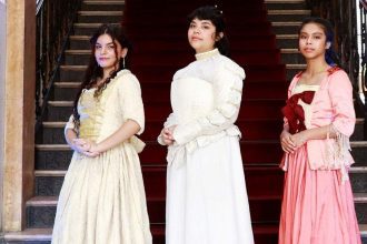Três mulheres em trajes de época posam em frente a escadaria do Palácio da Justiça.