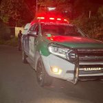 Viatura da Polícia Militar no local de uma ocorrência à noite, com luzes de emergência acesas.
