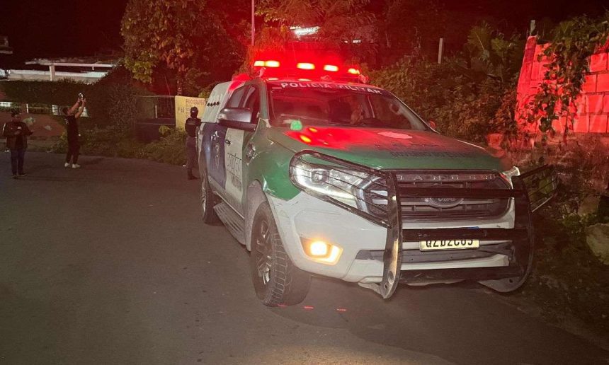 Viatura da Polícia Militar no local de uma ocorrência à noite, com luzes de emergência acesas.