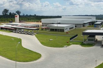 Vista aérea da fábrica da 3M em Manaus, com veículos e prédios industriais.