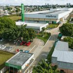 Vista aérea da fábrica da Intelbras em Manaus, com carros estacionados e prédios ao fundo.