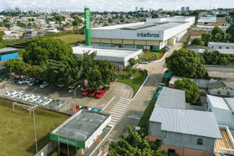 Vista aérea da fábrica da Intelbras em Manaus, com carros estacionados e prédios ao fundo.
