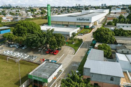 Vista aérea da fábrica da Intelbras em Manaus, com carros estacionados e prédios ao fundo.