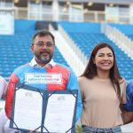 Wilson Lima em evento sobre editais culturais, com outras pessoas sorrindo e segurando documentos.