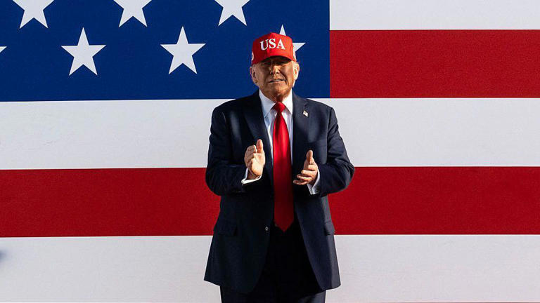 Imagem colorida mostra Donald Trump com boné vermelho e bandeira dos EUA ao fundo