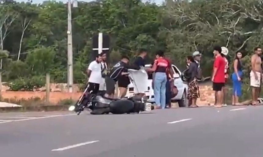 Acidente com moto em rodovia: veÃculo no chão, pessoas ao redor e vegetação ao fundo.