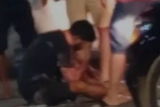 Acidente de trânsito com motociclista e carro. Pessoas ao redor do ferido.