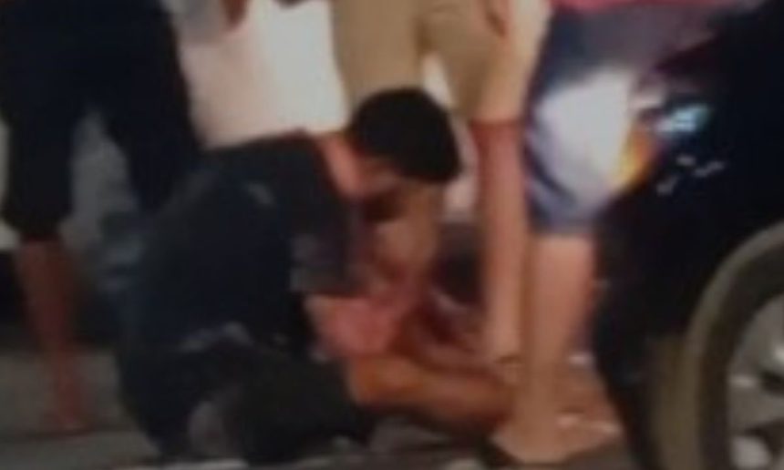 Acidente de trânsito com motociclista e carro. Pessoas ao redor do ferido.