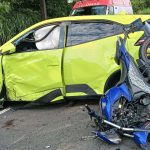 Acidente grave: carro amarelo danificado e moto azul destruída na pista.