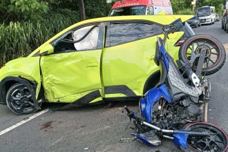 Acidente grave: carro amarelo danificado e moto azul destruída na pista.