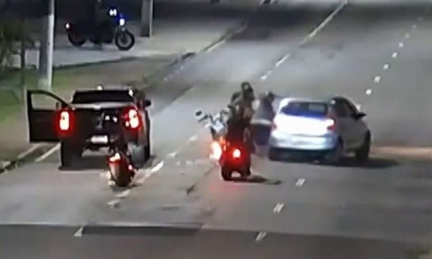 Agressão a policial federal em cena de rua à noite, com motos e carros.