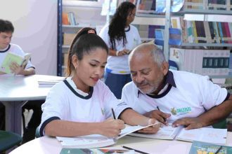 Alunos e professor em sala de aula, com foco em atividade de escrita e estudo.