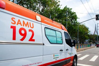 Ambulância do SAMU 192 em via pública, com sinalização de trânsito e vegetação ao fundo.
