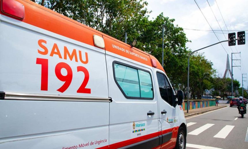 Ambulância do SAMU 192 em via pública, com sinalização de trânsito e vegetação ao fundo.