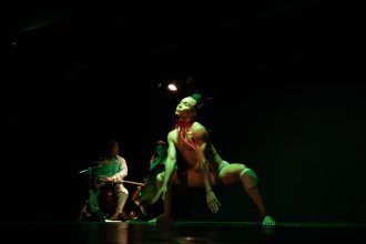 Apresentação de dança contemporânea no palco, com iluminação verde e foco no dançarino principal.