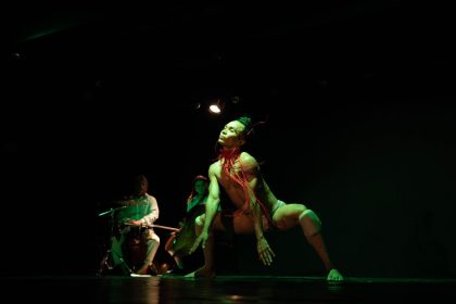 Apresentação de dança contemporânea no palco, com iluminação verde e foco no dançarino principal.