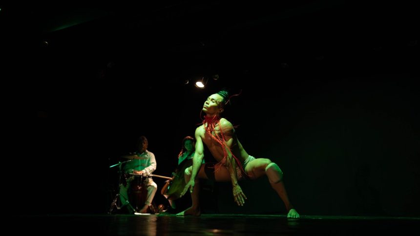 Apresentação de dança contemporânea no palco, com iluminação verde e foco no dançarino principal.