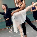 Bailarinos em ensaio de balé no palco, com foco em uma dupla em pose.