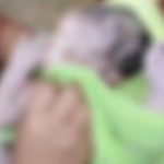 Bebê recém-nascido envolto em cobertor verde, sendo segurado por alguém.