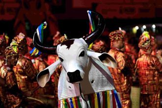 Boi-bumbá em apresentação no Sambódromo de Manaus, com adereços coloridos e público ao fundo.