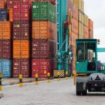Cais de porto com contêineres coloridos e veículos de transporte de carga.