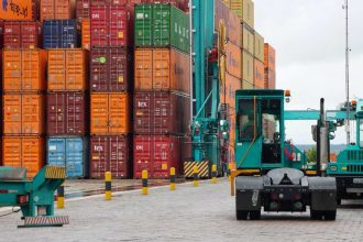 Cais de porto com contêineres coloridos e veículos de transporte de carga.