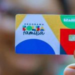 Cartão do programa Bolsa FamÃlia em mãos, com logo do programa e informações sobre benefÃcios.