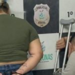 Casal preso em delegacia: mulher com algemas e homem com muletas.