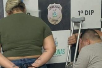 Casal preso em delegacia: mulher com algemas e homem com muletas.