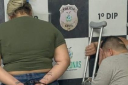 Casal preso em delegacia: mulher com algemas e homem com muletas.
