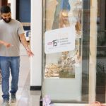 Casal sorrindo aponta para vitrine de loja de calçados em shopping.