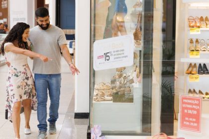 Casal sorrindo aponta para vitrine de loja de calçados em shopping.