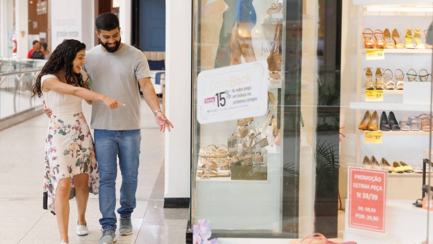 Casal sorrindo aponta para vitrine de loja de calçados em shopping.