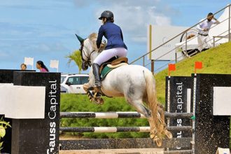 Cavaleira montando a cavalo branco saltando um obstáculo em competição de hipismo.