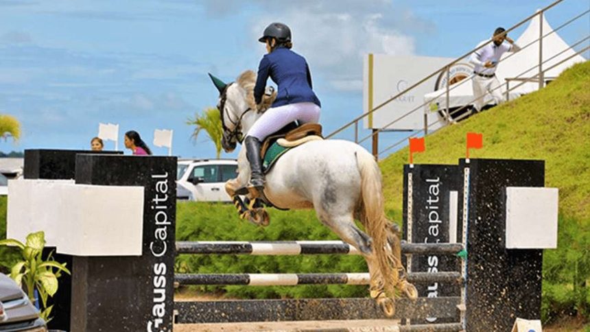 Cavaleira montando a cavalo branco saltando um obstáculo em competição de hipismo.