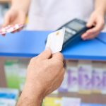Cliente pagando com cartão em farmácia, enquanto recebe medicamentos.