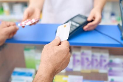 Cliente pagando com cartão em farmácia, enquanto recebe medicamentos.