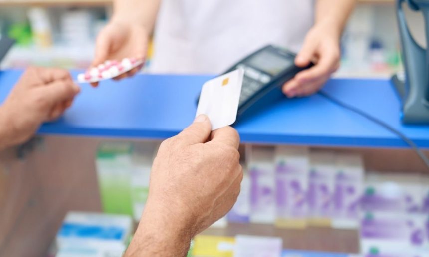 Cliente pagando com cartão em farmácia, enquanto recebe medicamentos.