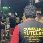 Conselheiro Tutelar em ação em ambiente noturno, lugares conhecidos como adegas, com pessoas ao fundo. Discagem para direitos humanos e denúncia.