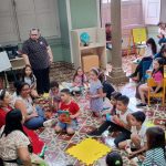 Crianças e adultos em biblioteca, evento de troca de livros e gibis.