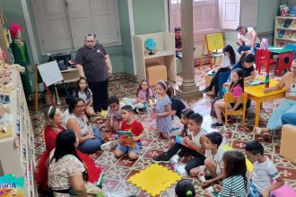 Crianças e adultos em biblioteca, evento de troca de livros e gibis.