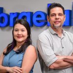 Dois profissionais sorrindo em frente ao logo da Sebrae, com inscrições para capacitação de artistas visuais amazônicos.