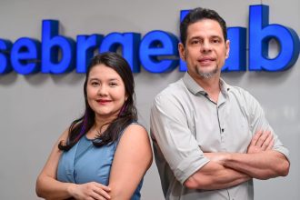 Dois profissionais sorrindo em frente ao logo da Sebrae, com inscrições para capacitação de artistas visuais amazônicos.