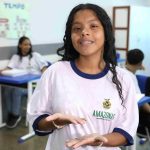 Estudante sorrindo e mostrando as mãos, em sala de aula
