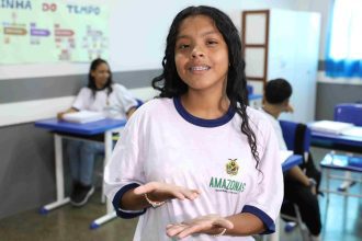 Estudante sorrindo e mostrando as mãos, em sala de aula