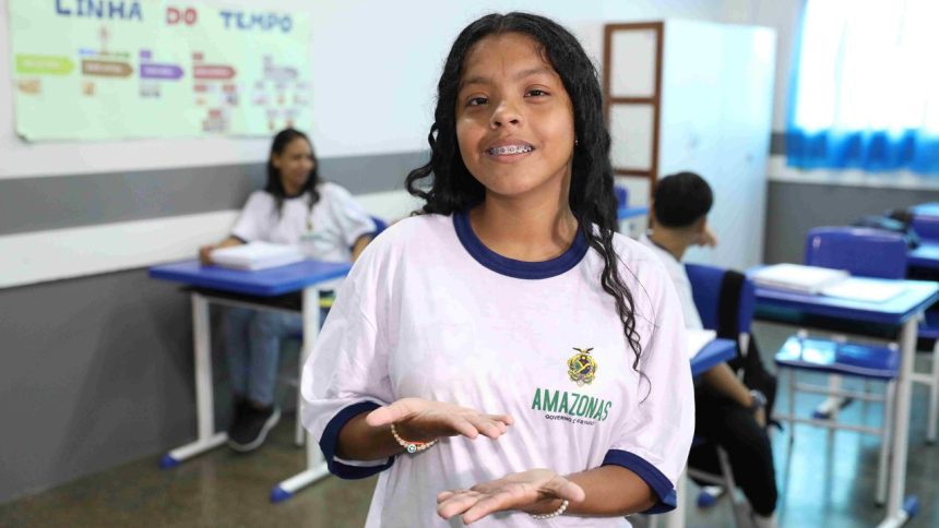 Estudante sorrindo e mostrando as mãos, em sala de aula