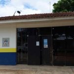 Fachada de delegacia com céu azul e árvores ao fundo.