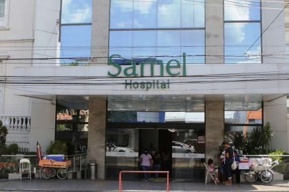 Fachada do Hospital Samel com entrada e letreiro verde. Pessoas em frente.