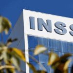 Fachada do prédio do INSS com o logotipo em destaque e folhagens em primeiro plano.