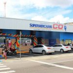 Fachada do Supermercado C.O com carros estacionados e pessoas na entrada.
